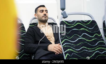 Geschäftsmann fährt mit öffentlichen Verkehrsmitteln und hört Musik. Medien. Mann im Anzug fährt allein im Bus. Mann geht zur Arbeit im Büro und hört Musik mit Stockfoto