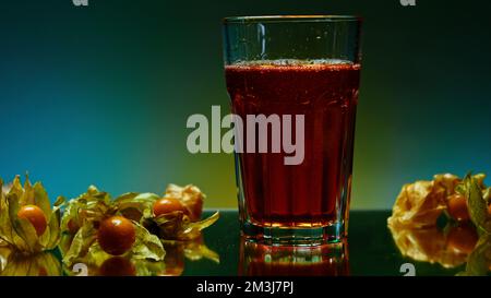 Erfrischendes kohlensäurehaltiges Getränk in transparentem Glas mit isolierten Beeren auf farbenfrohem Hintergrund. Clip-Material. Kühles Cola-Soda-Getränk an der Bar Stockfoto