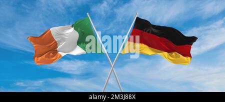 Zwei überkreuzte Flaggen Bundesrepublik Deutschland und Irland, die im Wind am bewölkten Himmel winken. Beziehungskonzept, Dialog, Reisen zwischen zwei Zählern Stockfoto