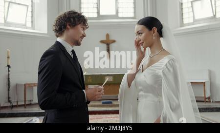 Traditionelle Hochzeitszeremonie mit Braut und Bräutigam in der Kapelle. Aktion. Ein Mann im Anzug, der ein Gelübde abgibt, und eine Frau im weißen Kleid, die sich die Tränen abwischt Stockfoto