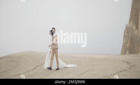 Wunderschönes junges Paar auf einem Berggipfel in Kappadokien. Aktion. Romantische Liebe von Mann und Frau, die Hand halten und in einem Morgennebel laufen Stockfoto