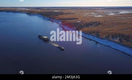 Luftaufnahme eines Frachtkahns, das Güter flussaufwärts transportiert. Clip. Fliegen über einem breiten Fluss mit einem Schiff und einem Kahn Stockfoto