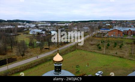 Luftaufnahme einer traditionellen orthodoxen Kirche in einem Sommerdorf. Clip. Fliegen Sie über die Landschaft mit kleinen Häusern Stockfoto