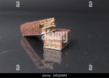 Schokoladenbonbons aus Waffelblättern und Schokoladenfüllende Pralinen-Ganache. Barkuchen in Schokoladenglasur auf schwarzem Hintergrund. Tag Der Schokoladenbonbons. Stockfoto