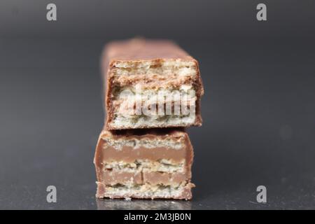 Schokoladenbonbons aus Waffelblättern und Schokoladenfüllende Pralinen-Ganache. Barkuchen in Schokoladenglasur auf schwarzem Hintergrund. Tag Der Schokoladenbonbons. Stockfoto