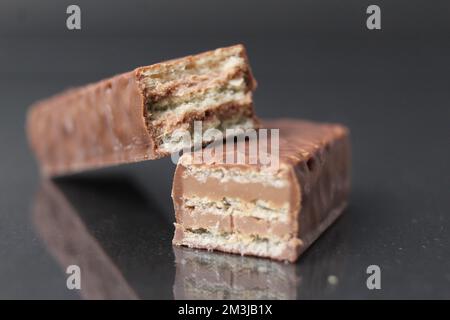 Schokoladenbonbons aus Waffelblättern und Schokoladenfüllende Pralinen-Ganache. Barkuchen in Schokoladenglasur auf schwarzem Hintergrund. Tag Der Schokoladenbonbons. Stockfoto
