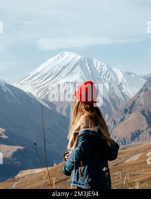 Ein Mädchen mit rotem Hut, das von hinten auf die Berge blickt Stockfoto