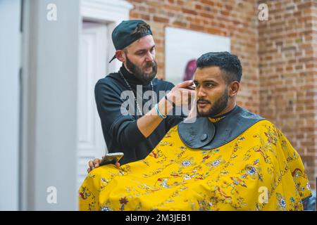 Ich brauche eine neue Frisur, einen Kunden, der auf dem Stuhl sitzt und einen Friseur, der ihm einen neuen Haarschnitt macht, einen Friseursalon. Hochwertiges Foto Stockfoto