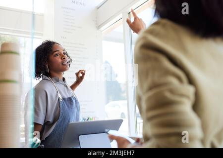 Der Gast zeigt auf die Speisekarte, während er mit einer Unternehmerin im Café spricht Stockfoto