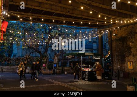 LONDON, ENGLAND - November 30 2022: Borough Market nahe London Bridge. Ein Mann verkauft Weihnachtsgeschenke auf dem Markt unter dem Licht der Girlanden bei einer Erkältung Stockfoto