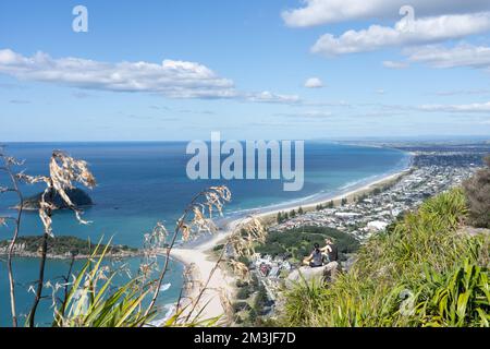 Tauranga Neuseeland - 7 2022. April; Junges Paar sitzt auf einem Felsen auf dem Gipfel des Mount Maunganui in der Morgensonne Stockfoto