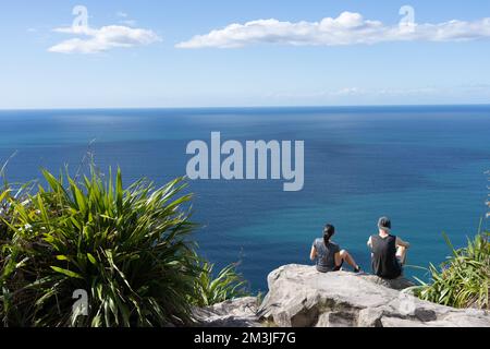 Tauranga Neuseeland - 7 2022. April; Junges Paar sitzt auf einem Felsen auf dem Gipfel des Mount Maunganui in der Morgensonne Stockfoto