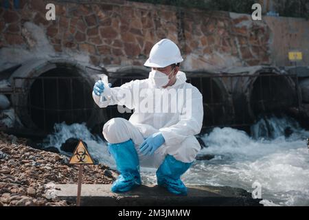 Ökologe entnehmen wassertoxische Chemikalien aus dem Fluss mit Reagenzglas und weisen weißen Rauch auf Stockfoto