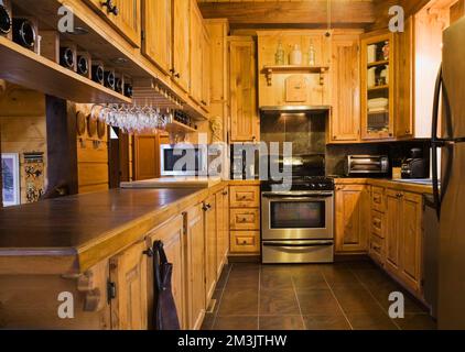 Holzschränke in der Küche mit Edelstahlgeräten in Stück sur Stück Blockhaus. Stockfoto
