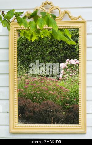 Gerahmter Spiegel an der Seite des Lagerschuppens reflektiert im Sommer die Pflanzen in einem landschaftlich gestalteten Garten im Garten. Stockfoto