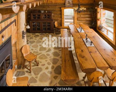 Blick von oben auf einen geteilten Holztisch und Bänke im Speisesaal in einer rustikalen Blockhütte. Stockfoto