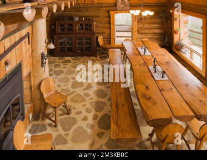 Blick von oben auf einen geteilten Holztisch und Bänke im Speisesaal in einer rustikalen Blockhütte. Stockfoto