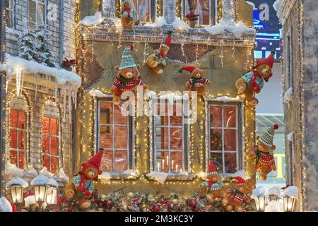 teddybären in Weihnachtsmann-Hüten krabbeln an der Wand eines zu Weihnachten dekorierten Hauses. Das Konzept von Weihnachten und Neujahr. Stockfoto