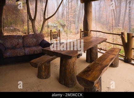 Esstisch aus gebeiztem und lackiertem Holz und Bänke im Sonnenzimmer, das an eine rustikale Blockhütte angeschlossen ist. Stockfoto