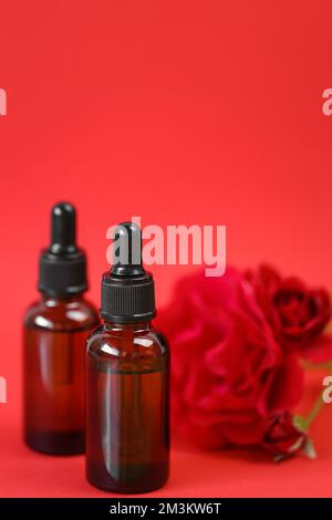 Rosenöl. Organisches Rosenöl in braunen Glasflaschen und rotes Rosenöl auf rotem Hintergrund. Aromatherapie und Kosmetik Stockfoto