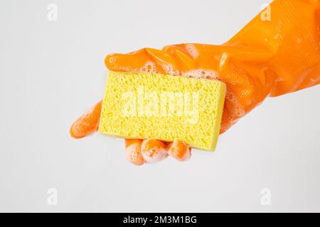 Reinigungskonzept, Hand in orangefarbenen Gummihandschuhen und gelber Schwamm mit Schaumstoff zur Reinigung. Stockfoto