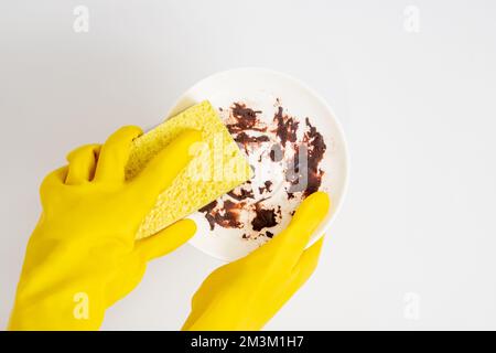 Geschirrspülkonzept, Hände in Gummihandschuhen, um den gelben Schwamm zu halten und das Geschirr zu waschen. Stockfoto