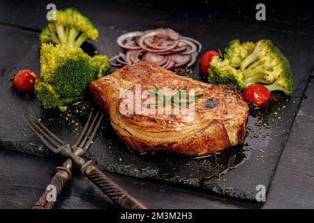 Schmackhaftes BBQ-Schweinelende mit Gemüse auf einem schwarzen Steinbrett. Schweinebraten und Brokkoli Stockfoto