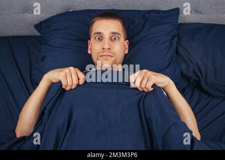 Direkt in den Rahmen schauen. Ein hübscher junger Mann, der sich hinter einer Decke versteckt, schaut zur Seite. Blickrichtung in verschiedene Richtungen. Stockfoto