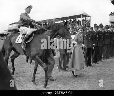 Aktenfoto von 07-10-1957 von der Queen, die ihre Oaks-Gewinnerin Carrozza führt, mit Lester Piggott. Zweifellos einer der größten Jockeys aller Zeiten, Piggott's Classic Hol umfasste neun Derby-Siege und wurde 11 Mal zum Champion Jockey gekrönt. Es war 1954 an Bord, niemals die sagen, dass er seinen ersten Derby-Sieg zustande brachte. Acht Jahre später erwies sich 1966 mit 191 Gewinnern als seine beste Saison. Er starb im Alter von 86 Jahren. Ausgabedatum: Freitag, 16. Dezember 2022. Stockfoto