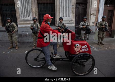 Lima, Peru. 15.. Dezember 2022. Ein Mann auf einem Cargo Bike fährt an einer Gruppe bewaffneter Soldaten im Zentrum von Perus Hauptstadt vorbei. Laut Regierungsquellen sind in verschiedenen Teilen Perus Menschen bei immer gewalttätigeren Protesten gegen die Vertreibung von Präsident Castillo ums Leben gekommen. Tausende forderten den Rücktritt von Castillos Nachfolger Boluarte sowie die Auflösung des parlaments, vorgezogene Neuwahlen und die Freilassung des inhaftierten Ex-Präsidenten. Kredit: Lucas Aguayo Araos/dpa/Alamy Live News Stockfoto