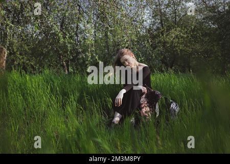 Frau, die direkt starrt und in großem Gras sitzt, malerische Fotografie Stockfoto