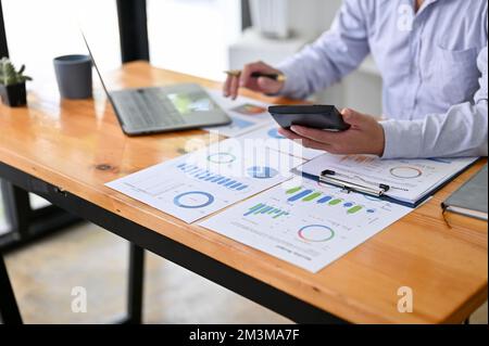 Professioneller asiatischer Geschäftsmann oder Finanzberater mit Taschenrechner, der an Finanzdatenberichten an seinem Schreibtisch arbeitet. Zugeschnittenes Bild Stockfoto