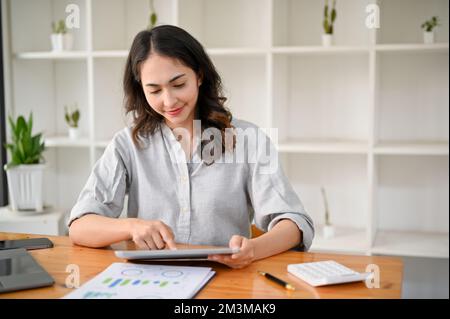 Charmante und professionelle asiatische Geschäftsfrau oder Managerin, die ein digitales Tablet an ihrem Schreibtisch verwendet. Stockfoto