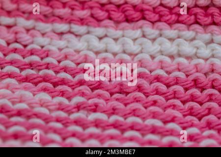 Unschärfe-Effekt auf abstraktem Makrohintergrund eines handgestrickten rosa-weißen Stoffes in einem Strumpfmuster Stockfoto