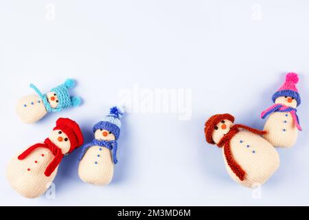 Gestrickte Schneemänner in farbenfrohen Mützen und Schals auf blauem Hintergrund. Das Konzept von Weihnachten, Neujahr und Wintermärchen. Flach verlegt Stockfoto