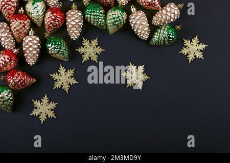 Weihnachtsdekorationen in Form von goldenen, roten, grünen Zapfen und Schneeflocken auf schwarzem Hintergrund mit einem Platz für Text. Draufsicht. Stockfoto