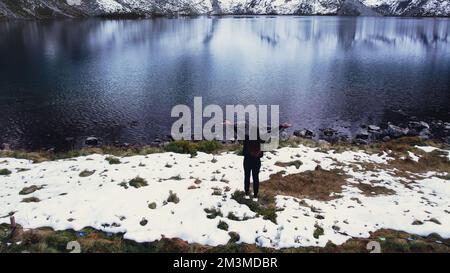 Glückliche Frau, die die Czarny Staw pod Rysamy oder den Black Pond See in der Nähe der Morskie Oko Snowy Mountain Hut in den polnischen Tatry Bergen genießt, Blick auf die Drohne, Zakopane, Polen. Einheit mit Natur Luftaufnahme der wunderschönen grünen Hügel und Berge in dunklen Wolken und Reflexion auf dem See Morskie Oko. Reiseziel 4K Stockfoto