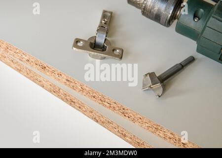 Montagewerkzeuge für Möbelbeschläge. Ein angeschlossenes Scharnier an einem Schrank. Stockfoto