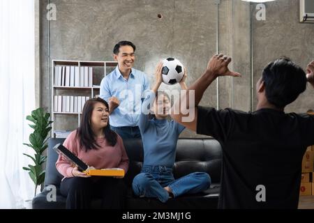 Freunde sehen sich Sport im Fernsehen an, jubeln und feiern. Fröhliche, vielfältige asiatische Fans setzen sich mit Popcorn und Drinks auf die Couch Stockfoto