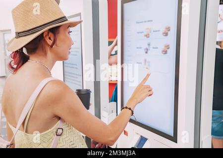 Eine Kundin nutzt ein Touchscreen-Terminal oder einen Selbstbedienungskiosk, um in einem Fast-Food-Restaurant zu bestellen. Automatisierte maschinelle und elektronische Zahlung Stockfoto