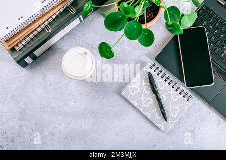 Moderner Bürotisch mit Laptop, Smartphone und anderem Zubehör mit einer Tasse Kaffee Stockfoto