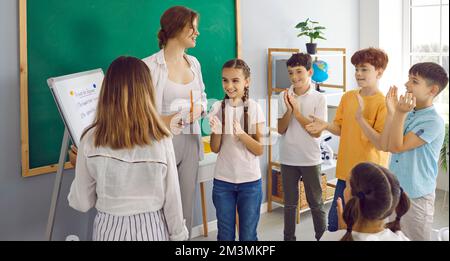 Kinder, Teenager und Grundschullehrer applaudieren einer Klassenkameradin, die die richtige Lösung schrieb Stockfoto