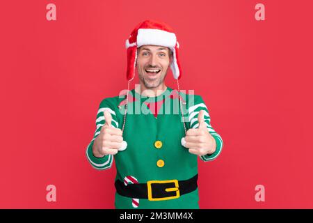 Staunender Mann im Elf Kostüm. weihnachtsmann im weihnachtsmann Hut auf rotem Hintergrund. Frohes neues Jahr. Stockfoto