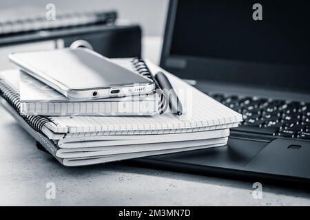 Bürotisch – Stapel von Notebooks, Mobiltelefon mit Laptop Stockfoto