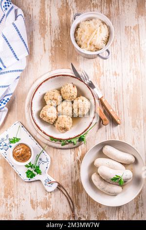 Traditionelle bayerische Küche - Weiße Kalbswurst mit eingelegtem Weißkohl (Sauerkraut) und Brotknödeln mit Senfsauce Stockfoto