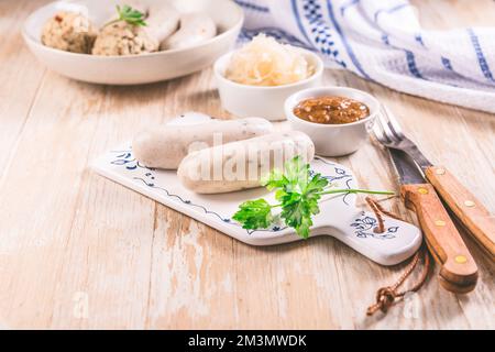 Traditionelle bayerische Küche - Weiße Kalbswurst mit eingelegtem Weißkohl (Sauerkraut) und Brotknödeln mit Senfsauce Stockfoto