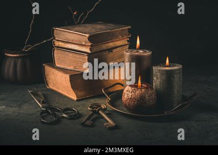 Ein Haufen alter antiker Bücher mit Kerzen und alten rostigen Schlüsseln im Vintage-Stil auf schwarzem Hintergrund Stockfoto