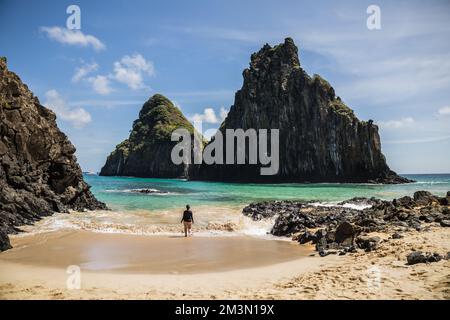 Die Frau, die am Strand steht und auf die Klippen schaut. Cacimba do Padre, Fernando de Noronha, Brasilien. Stockfoto