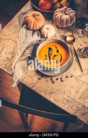 Kürbiscremesuppe mit Kürbiskernen auf einem dekorierten Küchentisch Stockfoto