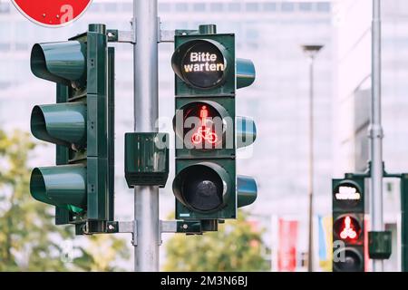 Rote Ampel für Fußgänger und Radfahrer und die Inschrift - bitte warten Sie auf Deutsch. Unfälle und Verkehrsregeln Stockfoto